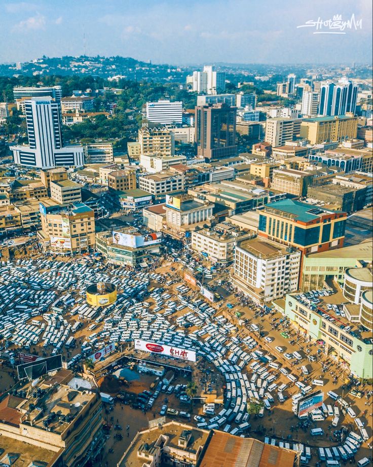Aerial view of Kampala city with busy taxi park full of white minibuses, surrounded by commercial buildings, bustling streets, and green hills in the background, captured by Roadrave Tours and Travel showcasing vibrant Ugandan urban life.