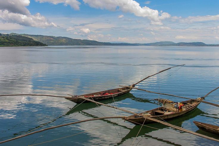 Traditional wooden fishing boats floating on the calm waters of Lake Kivu surrounded by hills and blue skies, highlighting Rwanda’s serene lakeside culture with Rordrave Tours and Travel.