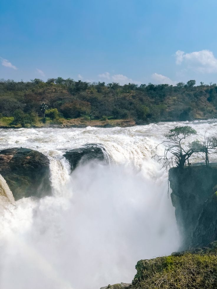 Murchison Falls waterfall in Uganda cascading over rocky cliffs with mist and lush green vegetation, photographed by Roadrave Tours and Travel showcasing powerful natural beauty and safari adventure.