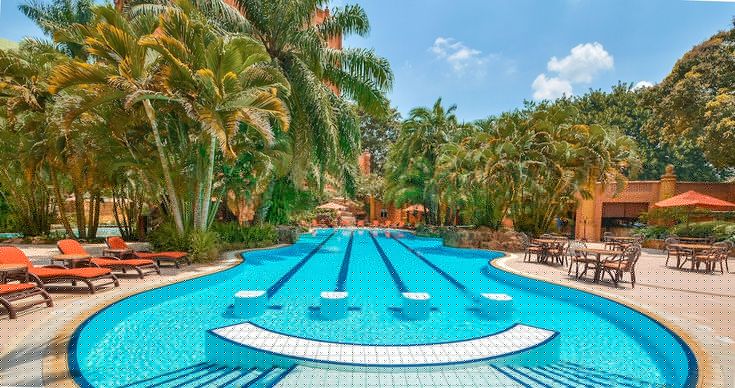 Luxury tropical resort infinity pool surrounded by palm trees and thatched roof villas - Road Rave Tours