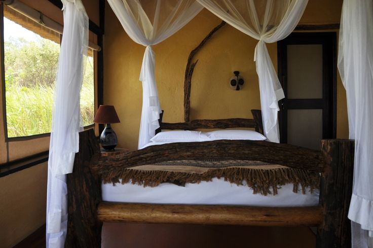 Rustic luxury safari bedroom interior with wooden bed and mosquito netting at Kyambura Gorge Lodge - Road Rave Tours