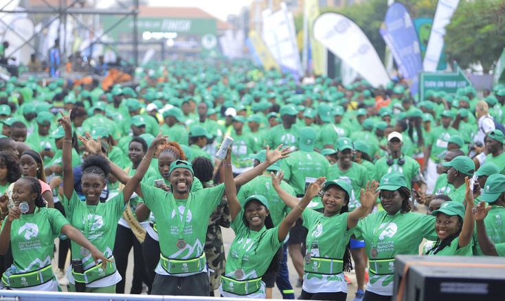 A lively crowd of participants wearing matching green Tusker Lite Rwenzori Marathon t-shirts, green caps, and medals celebrating together at the finish line with Roadrave Tours and Travel in Kasese, Uganda.