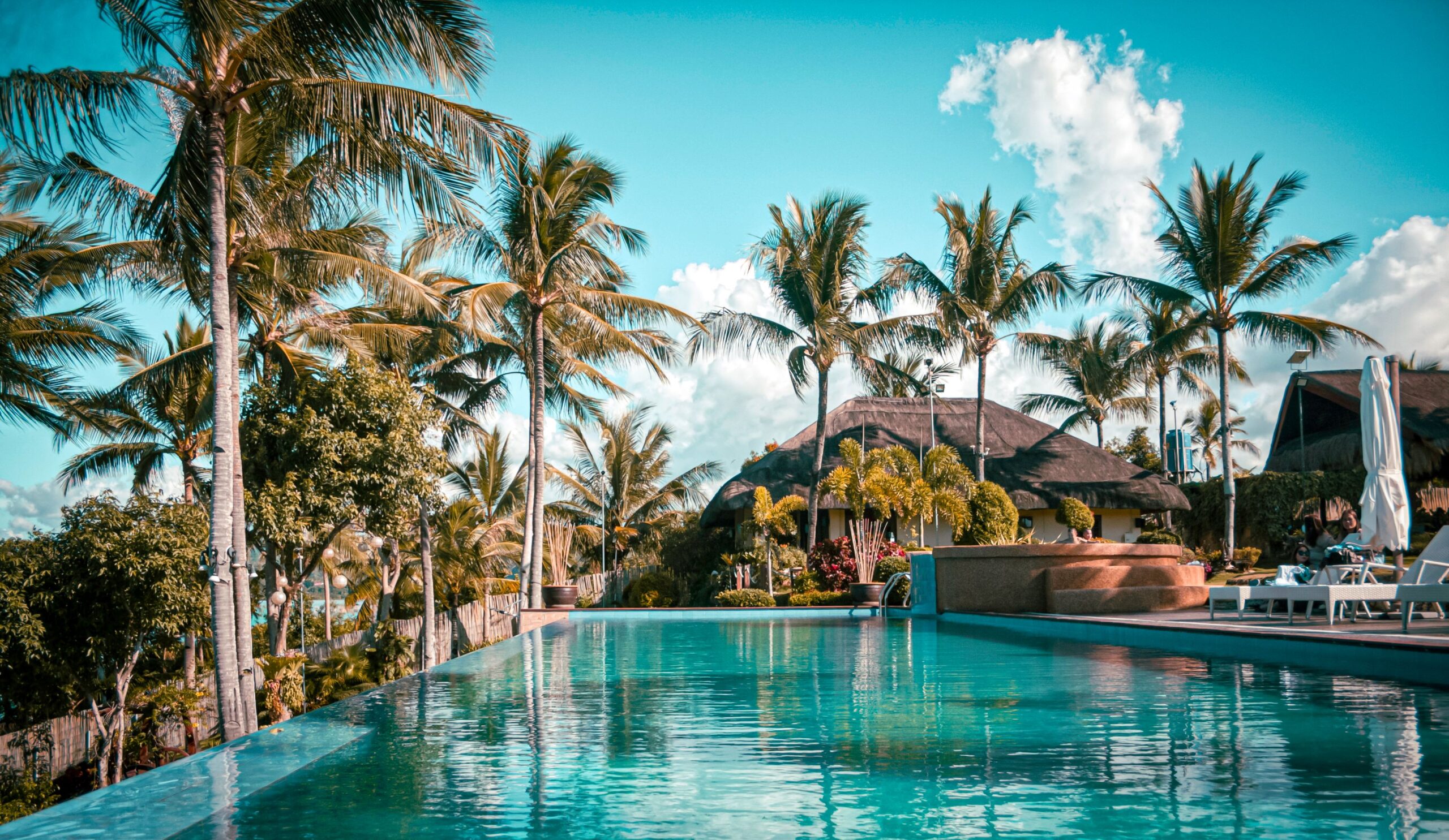 Luxury tropical resort infinity pool surrounded by palm trees and thatched roof villas - Road Rave Tours